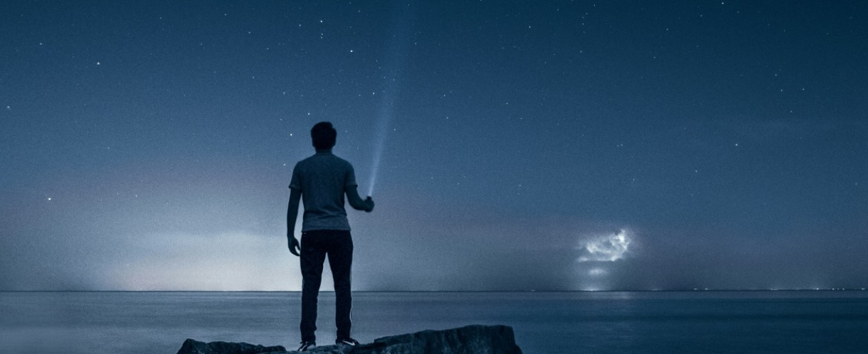 Image of a man looking out across the sea at night